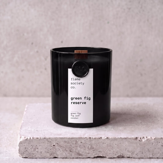 Green Fig Reserve candle hero — black glass vessel with wooden wick, green fig, fig leaf and coconut — Flame Society Co.