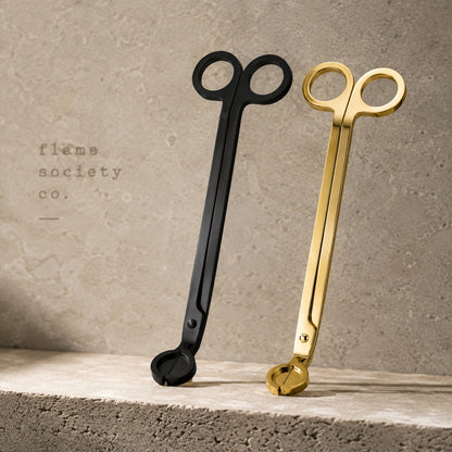 Flame Society Co. wick trimmers in matte black and polished gold leaning against travertine stone