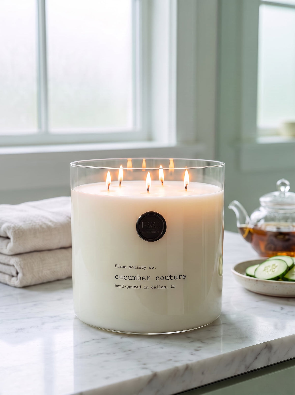 Cucumber Couture XL 150oz statement candle in a clear glass vessel in a marble spa bathroom — Flame Society Co.