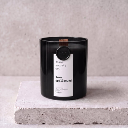 Love Spellbound candle hero — black glass vessel with wooden wick, cherry blossom, peach and jasmine — Flame Society Co.