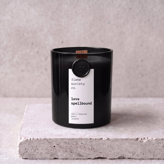 Love Spellbound candle hero — black glass vessel with wooden wick, cherry blossom, peach and jasmine — Flame Society Co.