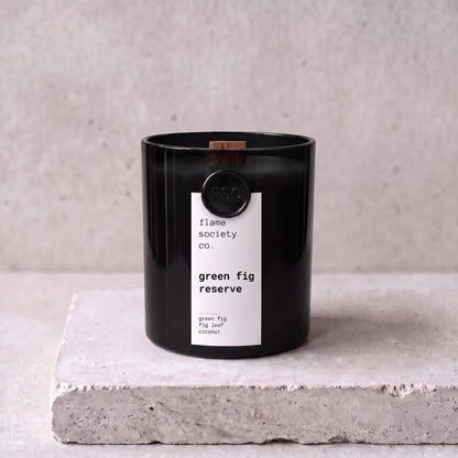 Green Fig Reserve candle hero — black glass vessel with wooden wick, green fig, fig leaf and coconut — Flame Society Co.