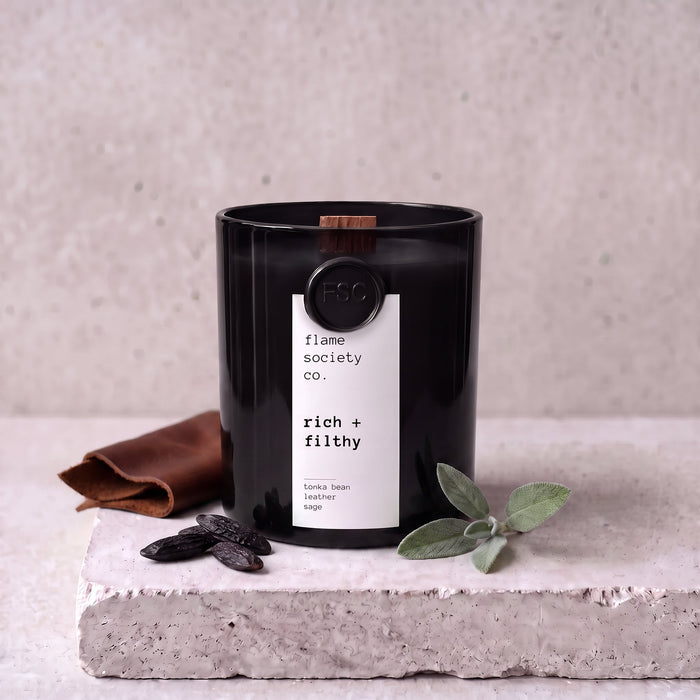Rich + Filthy candle styled with tonka bean, leather and sage on concrete — Flame Society Co.
