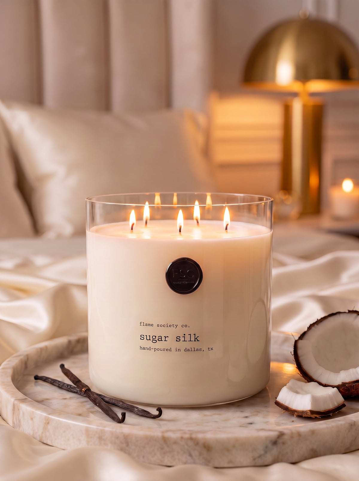 Sugar Silk XL 150oz statement candle in a clear glass vessel in a warm cream bedroom — Flame Society Co.