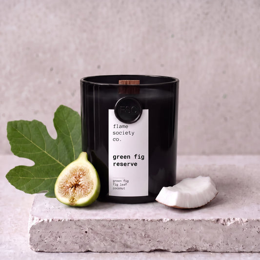 Green Fig Reserve candle styled with green fig, fig leaf and coconut on concrete — Flame Society Co.