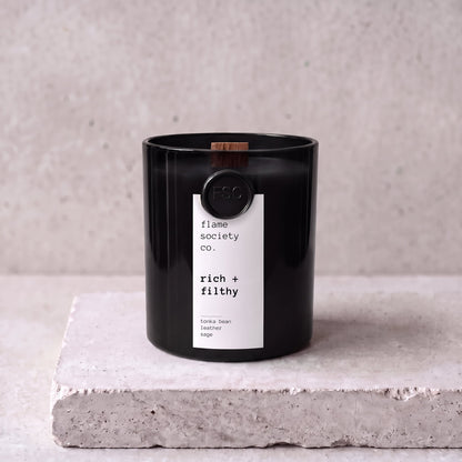 Rich + Filthy candle hero — black glass vessel with wooden wick, tonka bean, leather and sage — Flame Society Co.