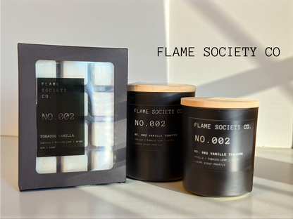 Two black candles with wooden lids and a box labeled 'Flame Society Co.' on a light background.