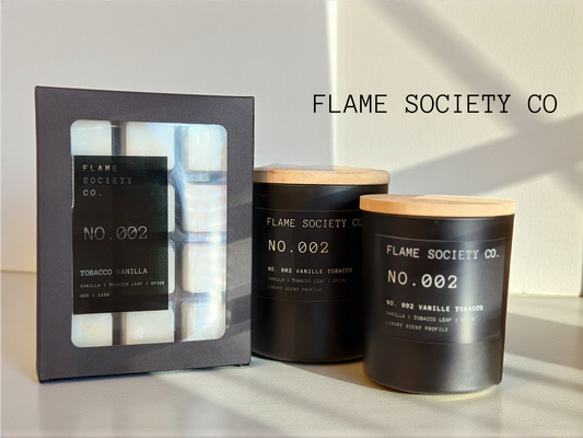 Two black candles with wooden lids and a box labeled 'Flame Society Co.' on a light background.