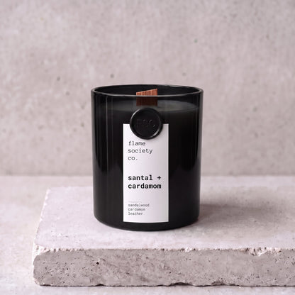 Santal + Cardamom candle hero — black glass vessel with wooden wick, sandalwood, cardamom and leather — Flame Society Co.
