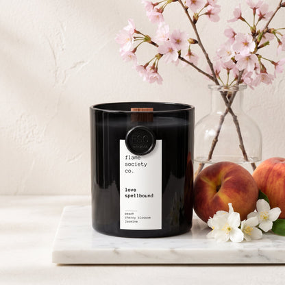 Flame Society Co. Love Spellbound candle in black glass vessel with cherry blossom, peach and jasmine styling.