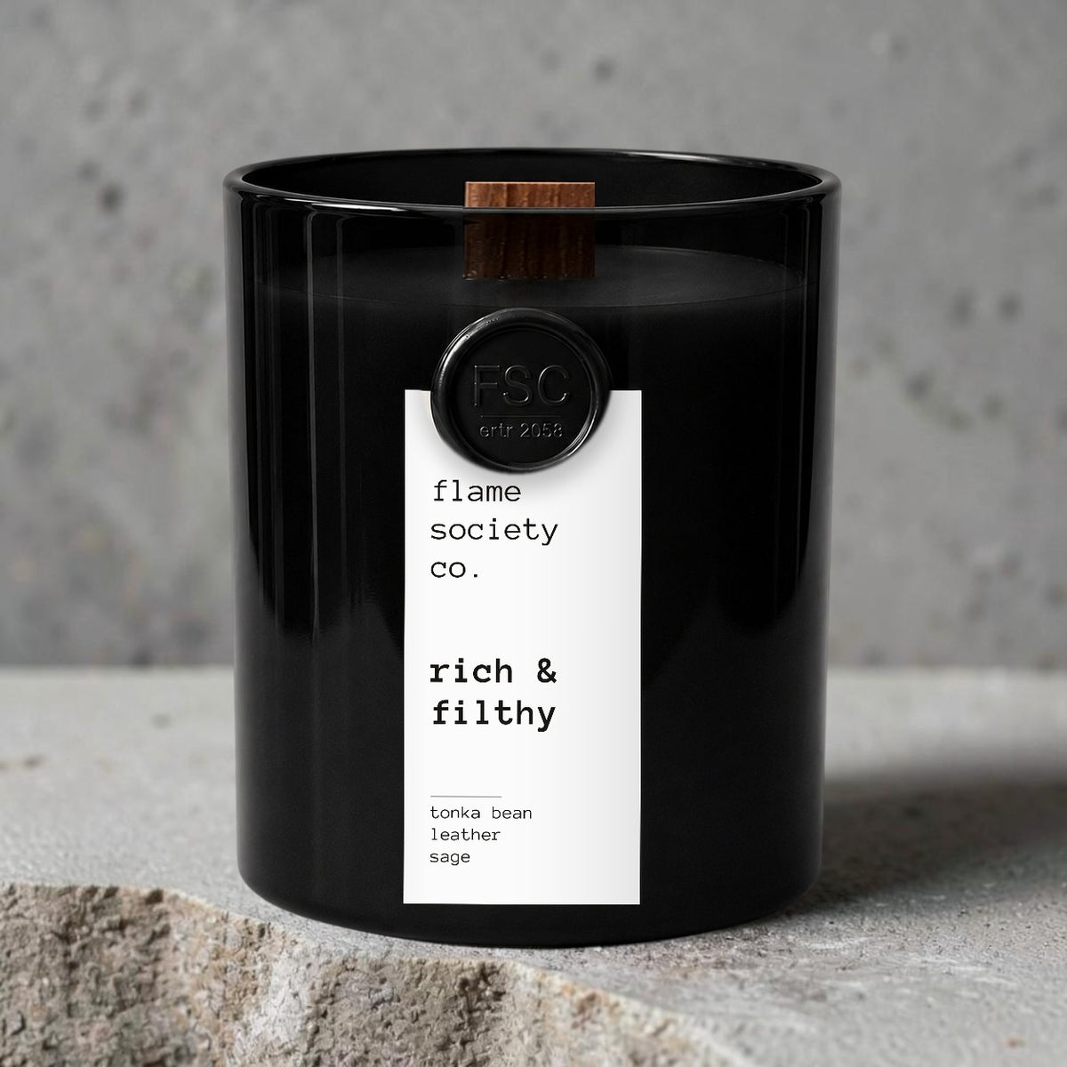 Flame Society Co. Rich & Filthy candle in black glass vessel with tonka bean, leather and sage notes on concrete.