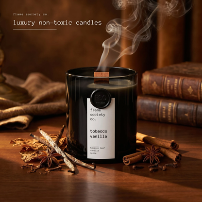 Candle labeled 'tobacco vanilla' from Flame Society Co. on a wooden surface with cinnamon sticks and star anise.