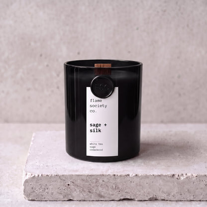 Sage + Silk candle hero — black glass vessel with wooden wick, white tea, sage and cedarwood — Flame Society Co.