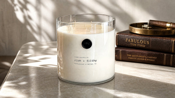 Flame Society Co. Big + Bougie 150oz Rich + Filthy statement candle in a clear glass vessel with a black wax seal on a marble table.