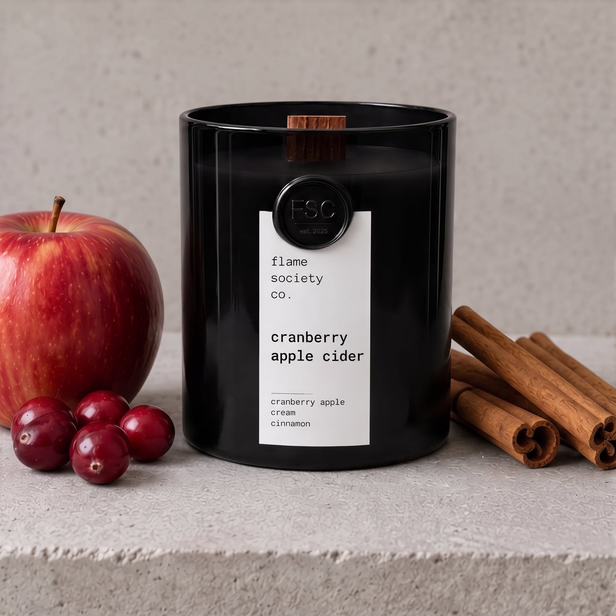Cranberry Apple Cider black jar candle with red apple, cranberries and cinnamon sticks on pale stone - Flame Society Co.