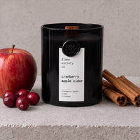 Cranberry Apple Cider black jar candle with red apple, cranberries and cinnamon sticks on pale stone - Flame Society Co.
