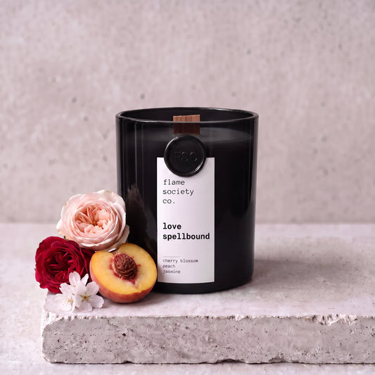 Love Spellbound candle styled with roses, peach and cherry blossom on concrete — Flame Society Co.