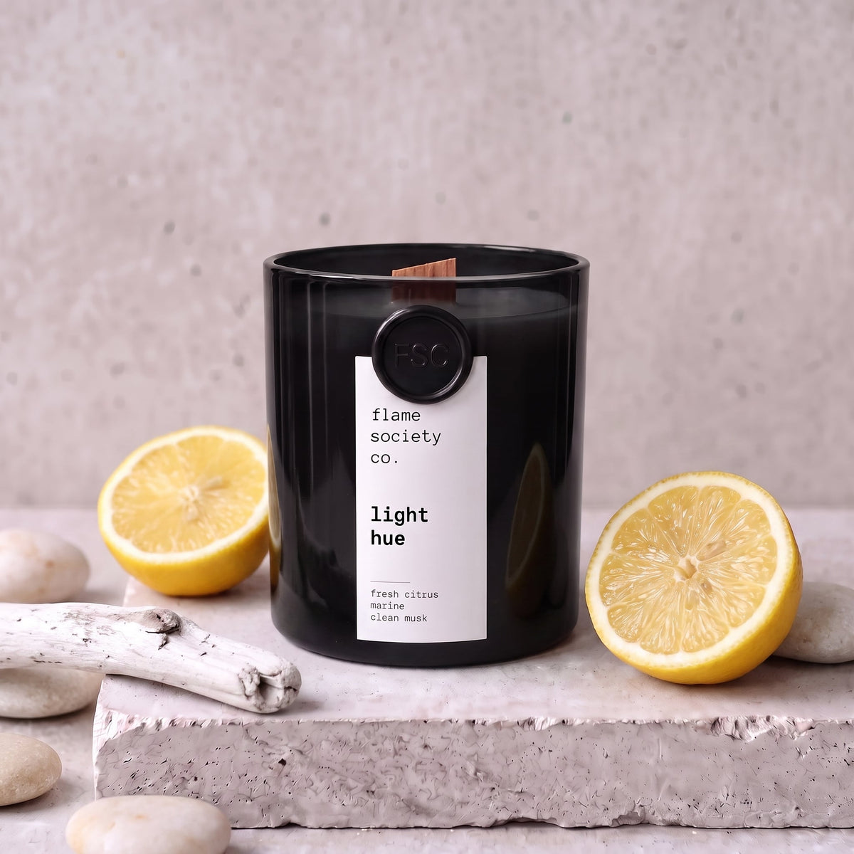 Light Hue candle styled with lemon, sea pebbles and driftwood on concrete — Flame Society Co.