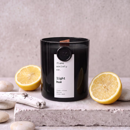 Light Hue candle styled with lemon, sea pebbles and driftwood on concrete — Flame Society Co.