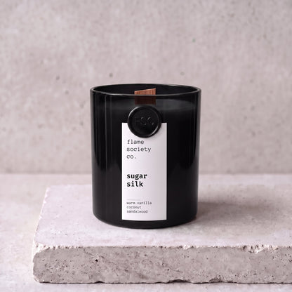 Sugar Silk candle hero — black glass vessel with wooden wick, warm vanilla, coconut and sandalwood — Flame Society Co.
